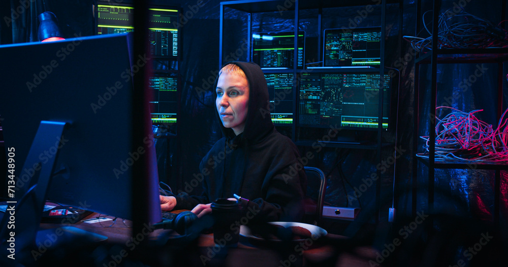 Caucasian joyful female hacker in hood sitting at table in technology ...