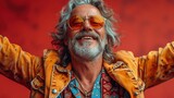 Fototapeta Tulipany - Exuberant senior man with silver hair and orange-tinted sunglasses, arms wide open in joy, wearing a vibrant jacket against a red backdrop.