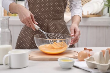 Wall Mural - Woman whisking eggs in bowl at table indoors, closeup