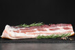 Piece of raw pork belly, rosemary and peppercorns on grey table
