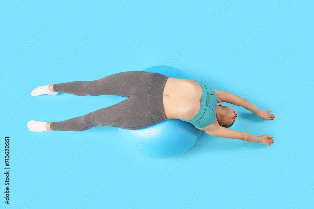 Young woman with fitball doing pilates on blue background, top view