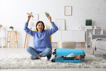 Canvas Print - Young woman with wooden plane, passport and suitcase sitting on floor at home