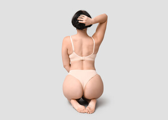 Body positive young woman in underwear sitting on light background, back view