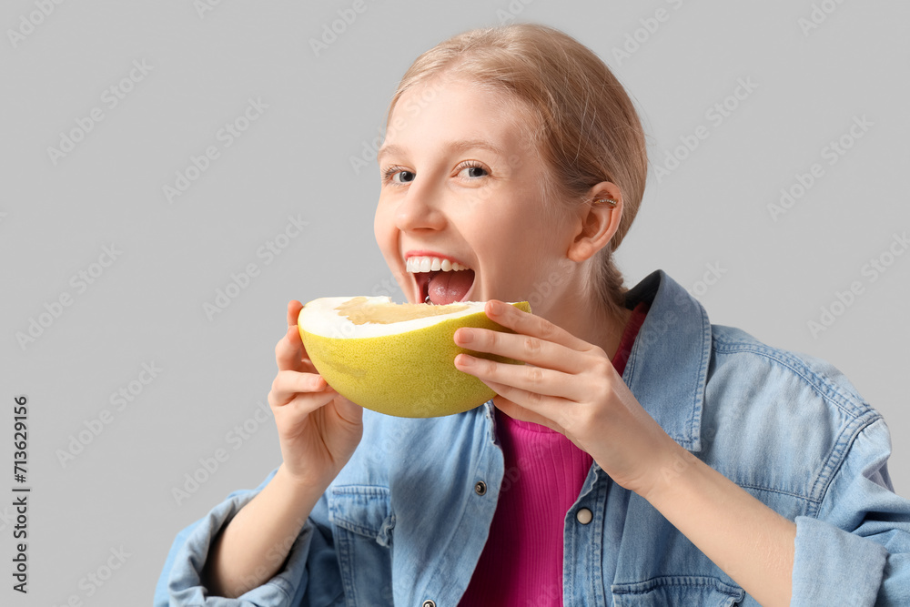 Young woman eating pomelo on light grey background, closeup