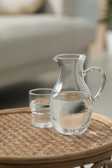 Wall Mural - Jug and glass with clear water on wicker surface against blurred background