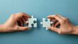 hand holding two jigsaw puzzle pieces in front of a blue background 
