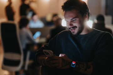 Happy young man using smart phone in cozy evening office environment.