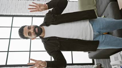 Wall Mural - Beaming young man, confidently pointing upwards with an eight sign, showcases joy from his cozy living room