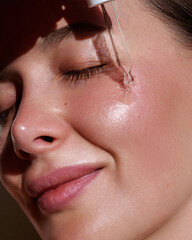 Serum. Moisturising and nourishing.  Close up beauty portrait of  beautiful woman with glowing skin is applying a vitamin c skincare product with a pipette dropper.