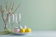 Easter table setting with pastel eggs, wine glasses, and cherry blossoms on pale green background. Easter celebration concept. Design for banner, poster, card with copy space. Minimalistic composition