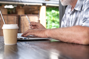 Wall Mural - Close-up view of senior man typing on laptop keyboard while using credit card for e-commerce purchases