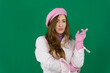 Attractive red-haired girl, stares in surprise and points her hands up to the free space young girl woman with a pink beret on her head France fashion on a green background chromakey. different