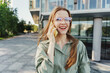 © muse studio - Smiling young woman talking on the phone in an urban setting.
