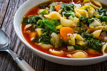 Wall Mural - Pistou soup Nice - broth with basil pesto, noodles and vegetables on wooden background in white bowl