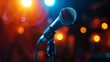 A single, sleek microphone stands on an illuminated stage, bathed in a dramatic spotlight with a dark, blurred background hinting at an expectant audience.