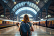 Rear view of a young woman with backpack on her back waiting at a large train station. Travel concept of vacation and holiday.