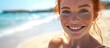 © The 2R Artificiality - Smiling red-haired lady in bikini with freckles applying sunscreen at beach.