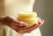 A woman's hand holding a jar of cosmetic cream.