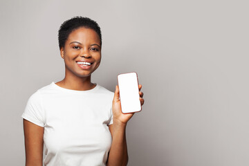 Positive woman showing smartphone with empty blank screen display. Model in white t-shirt with phone on gray studio wall background