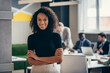 © gstockstudio - Confident African businesswoman smiling at camera while her colleagues working on background