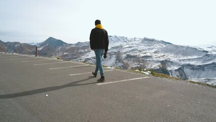 Wall Mural - Man traveler walks along Majestic Grossglockner Mountain Road in Austria, snow covered sharp peaks of the alpine mountains on background. Incredibly beautiful views in the Alpine mountains. Route in