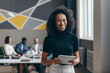 © gstockstudio - Smiling young African businesswoman holding digital tablet while her colleagues working