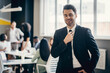 © gstockstudio - Smiling young businessman in formalwear adjusting necktie while his colleagues working on background