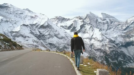 Wall Mural - Man traveler walks along Majestic Grossglockner Mountain Road in Austria, snow covered sharp peaks of the alpine mountains on background. Incredibly beautiful views in the Alpine mountains. Route in