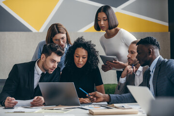 Wall Mural - Confident young business team looking at laptop while having group meeting in the office together