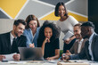 © gstockstudio - Happy young business team looking at laptop while having group meeting in the office together