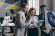 © gstockstudio - Three happy young people discussing business while their colleagues working on background