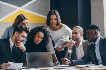 Canvas Print - Group of confident young business people looking at laptop while working at the modern office 