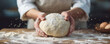 © zakiroff - Hands kneading dough on a floured wood surface, flour dust in motion, baking process, fresh ingredients visible, culinary art, home cooking, chef in apron, pastry preparation, kitchen table. Banner.