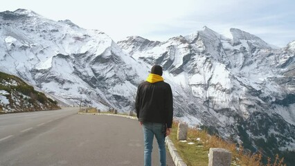 Wall Mural - Man traveler walks along Majestic Grossglockner Mountain Road in Austria, snow covered sharp peaks of the alpine mountains on background. Incredibly beautiful views in the Alpine mountains. Route in