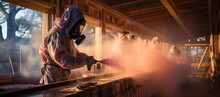 A Factory Worker Dressed In Protective Clothing Carefully Sprays Paint Indoors, Creating A Fiery Masterpiece