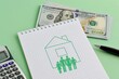 Concept of mortgage loan, home loan for building a house. Notepad with a picture of a house and a family icon on a green background with a calculator, US dollar bills and a pen