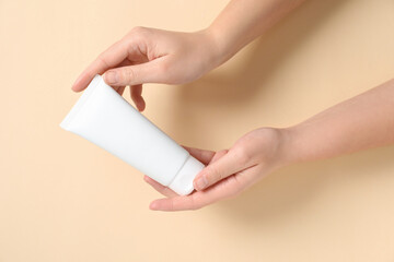 Poster - Woman with tube of hand cream on beige background, closeup