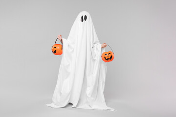 Wall Mural - Child in white ghost costume holding pumpkin buckets on light grey background. Halloween celebration