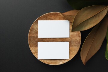 Canvas Print - Blank business cards and magnolia leaves on black background, flat lay. Mockup for design