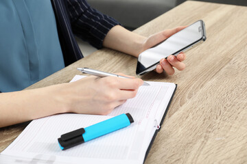 Wall Mural - Woman taking notes while using smartphone at wooden table, closeup