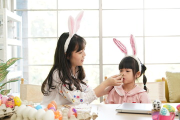 Mother and her daughter painting eggs. Happy family preparing for Easter. Cute little child girl wearing bunny ears.