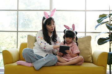 Mother and her daughter painting eggs. Happy family preparing for Easter. Cute little child girl wearing bunny ears.