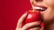 Woman trying to bite a fresh red apple. Red color copy space background. Healthy lifestyle concept