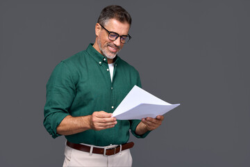 Wall Mural - Smiling elegant middle aged business man lawyer, happy older mature businessman professional financial adviser holding documents reading papers standing isolated on gray background.