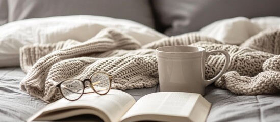 Sticker - Hygge concept: Comfortable home vibes. Beige sweater, tea or coffee mug, book, and glasses on gray bed. Long banner with space for design.