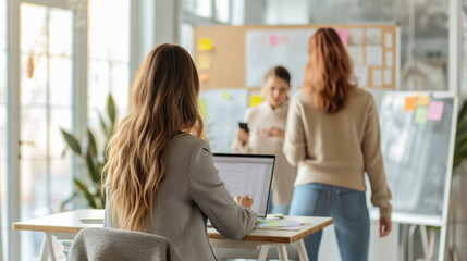 Wall Mural - Colleagues in a modern office setting, one from behind, working at a computer.