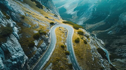 Poster -  an aerial view of a winding road in a mountainous area with snow on the ground and green grass on the side of the road and a cliff on the other side of the road.