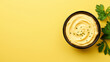 Bowl of hummus with greens and olive oil on yellow background, top view, copy space
