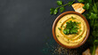 Bowl of hummus with greens and olive oil on dark background, top view, copy space