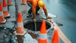 Worker over the open sewer hatch on a street near the traffic cones. Concept of repair of sewage, underground utilities, water supply system, cable laying, water pipe accident